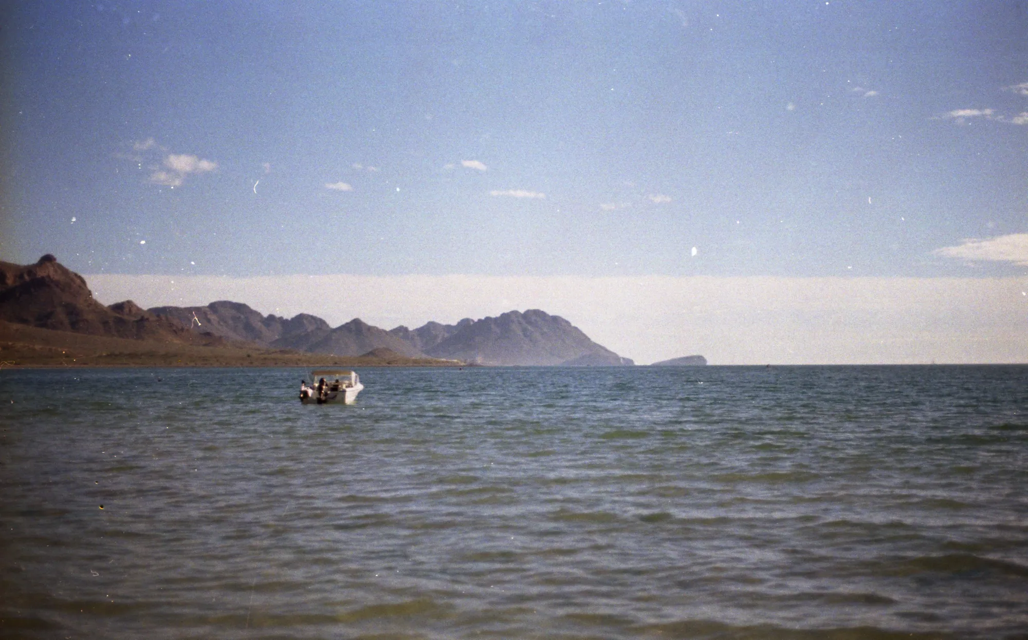 A small boat crossing calm water beneath distant mountains.