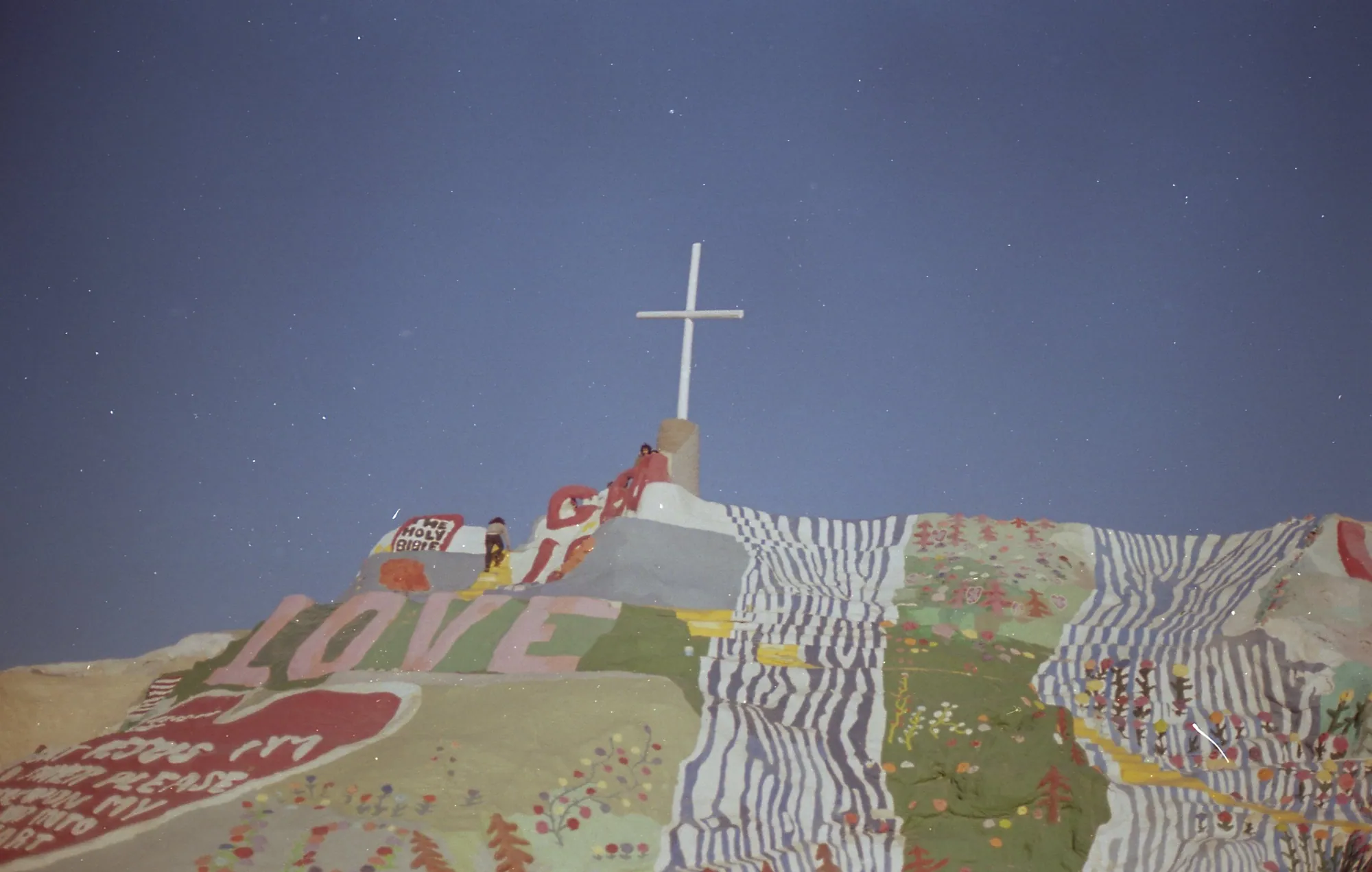 A white cross rising from the painted hillside.