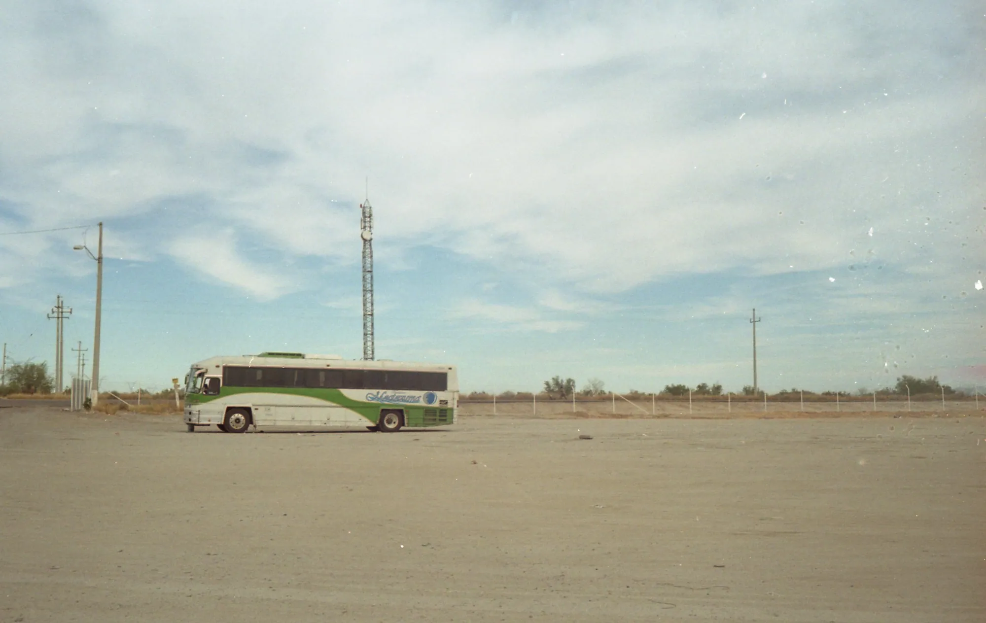 A solitary bus parked in a wide desert lot beneath a pale sky.