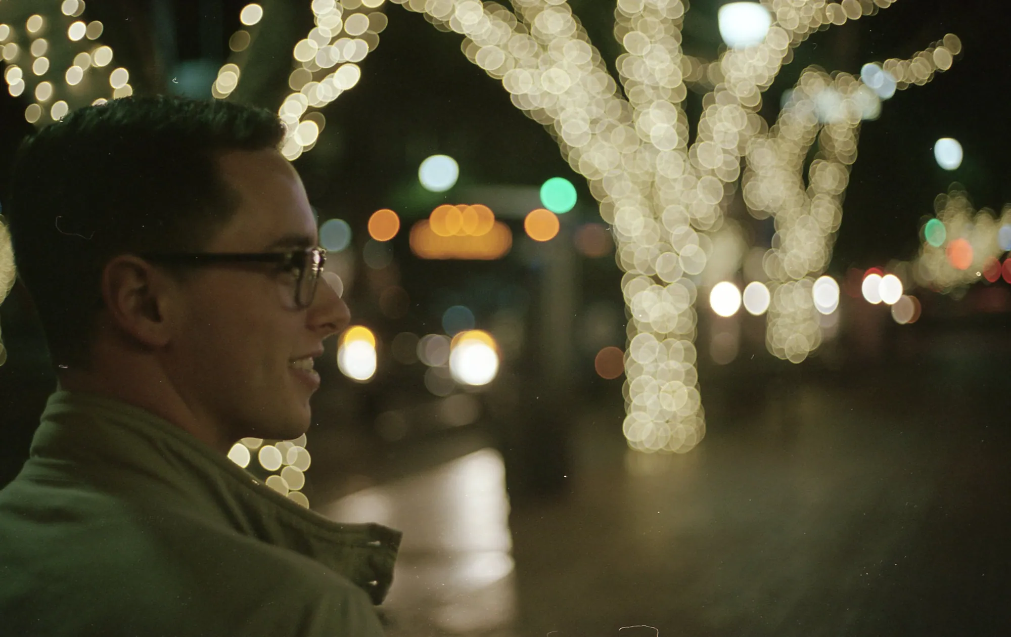 A person in profile against soft holiday lights at night.